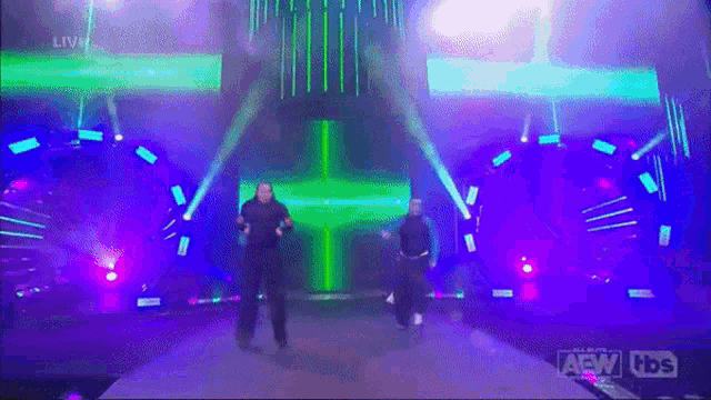 two men are dancing on a stage with a green cross in the background