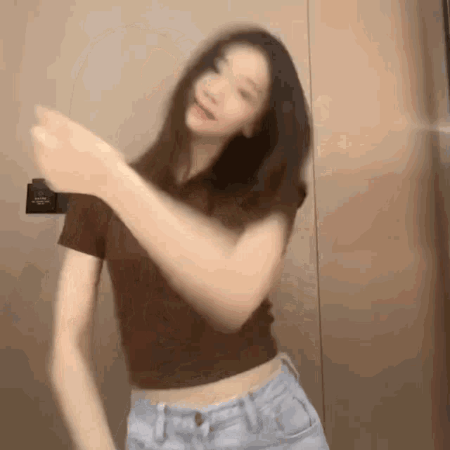 a woman in a brown crop top and jeans is dancing in front of a door .