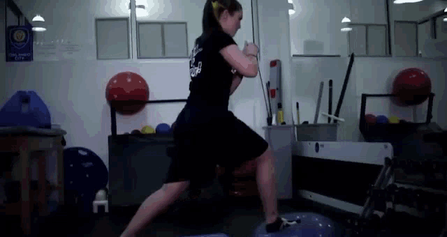 a woman is doing exercises in a gym while wearing a black shirt that says karate on it .