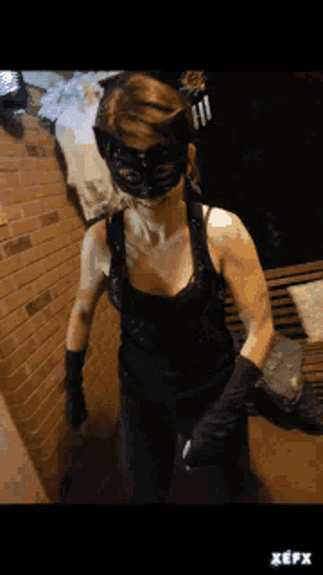 a woman in a cat mask and black gloves is standing in front of a brick wall