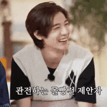 a young man wearing a black t-shirt and a white vest is smiling with korean writing behind him