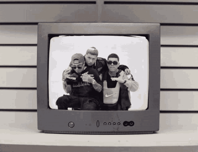three men pose for a picture on a tv screen with one wearing a nike bag