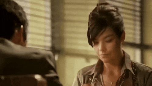 a woman is sitting at a table talking to a man in a chair .