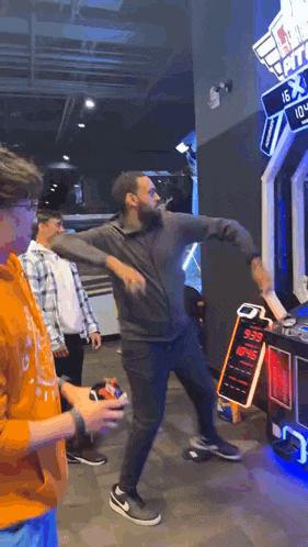 a man is dancing in front of a machine in an arcade while other people watch .
