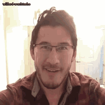 a man with glasses and a beard is smiling while taking a selfie .