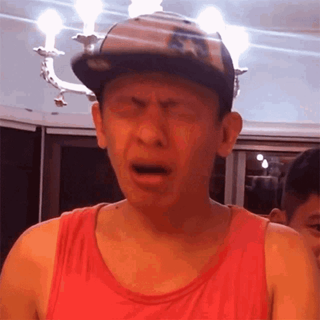 a man wearing a hat and a red tank top is making a face
