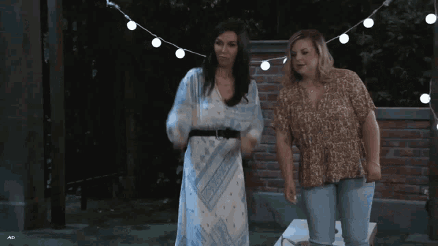 two women are standing next to each other in front of a brick wall and a string of lights