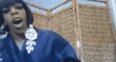 a woman wearing a blue robe and earrings is standing in front of a wicker screen .