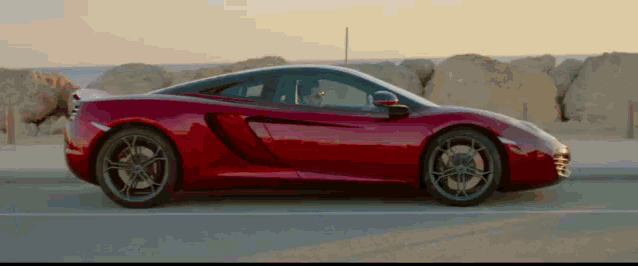 a red sports car is driving down a road near the ocean