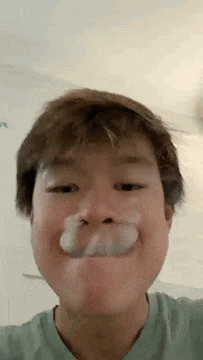 a young boy is making a funny face with his mouth open and a bubble in his nose .