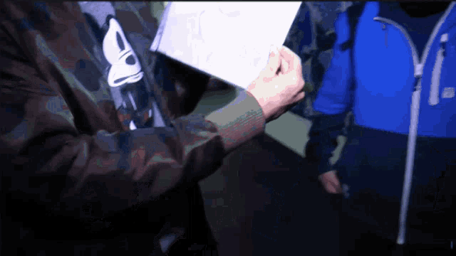 a person wearing a camo jacket holds a piece of paper in their hands