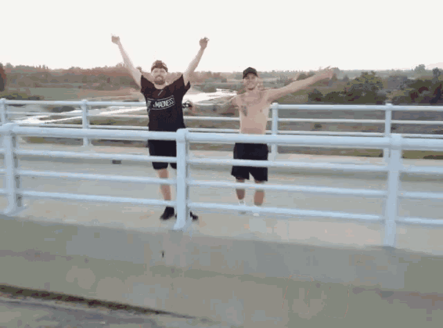 two men are standing on a bridge with their arms in the air and one of them has a shirt that says punks on it