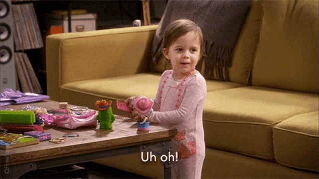 a little girl is playing with a toy on a table and says " uh oh "