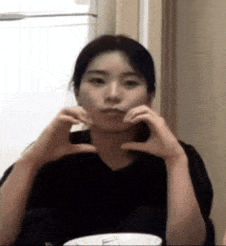 a woman is sitting at a table with a bowl of food and making a heart with her hands .
