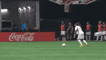 a soccer player kicking a soccer ball in front of a coca cola sign