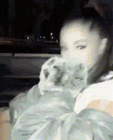 a black and white photo of ariana grande holding a cat in her arms .