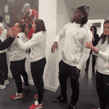 a group of people are dancing in front of a painting of a man in a red and black jersey that says allianz