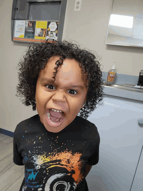a young boy with curly hair is making a funny face in front of a counter with a bottle of bug spray on it