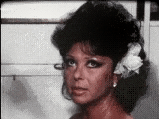 a woman with a flower in her hair is looking at the camera in a close up of her face .