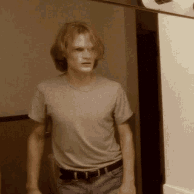 a young man standing in front of a mirror wearing a gray shirt