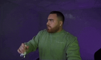 a man in a green sweater is holding a wii remote in his hand .