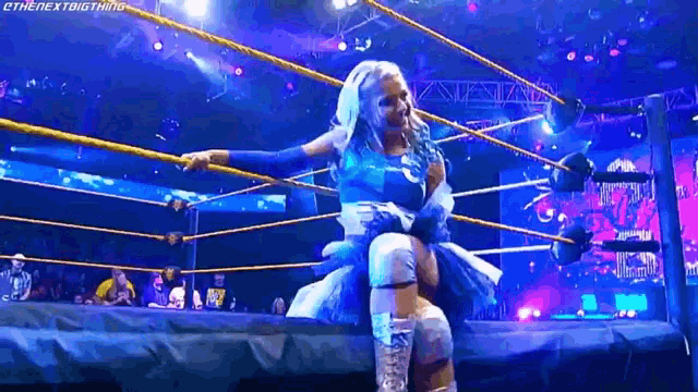 a woman in a blue dress is standing in a wrestling ring holding another woman .