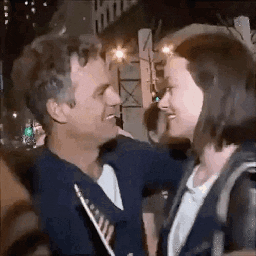 a man and a woman are hugging each other on a street at night .