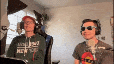 two men wearing headphones and sunglasses are sitting in front of microphones .
