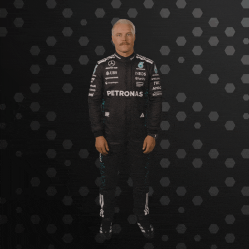 a man in a petronas racing suit stands in front of a black background