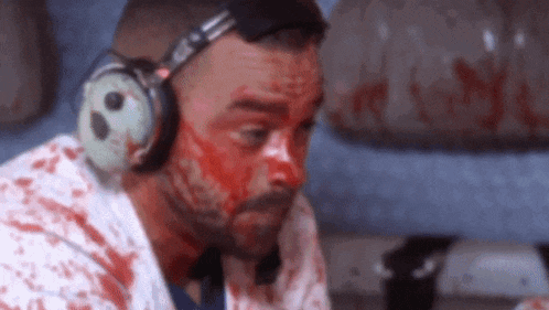 a man with blood on his face wearing headphones and a bloody shirt .