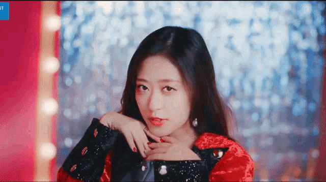 a woman in a red and black jacket is looking at the camera with her hand on her chest