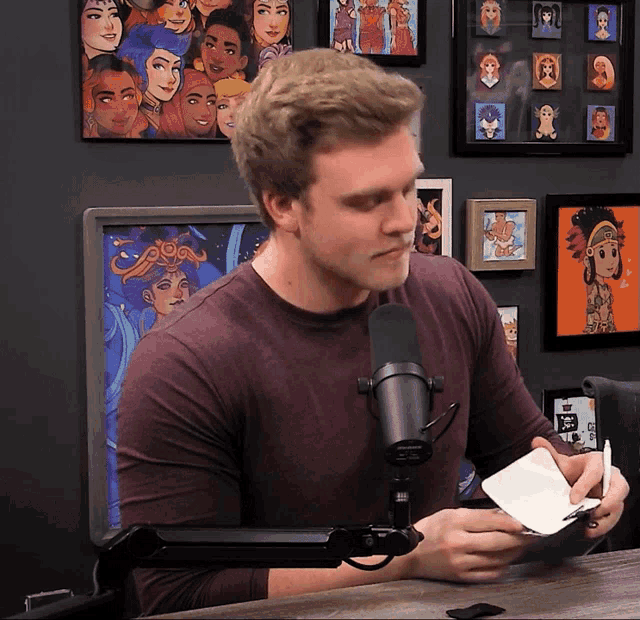 a man sitting in front of a microphone holding a piece of paper with a picture of a woman on the wall behind him