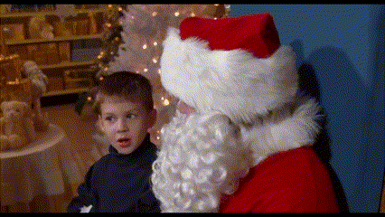 a little boy is talking to santa claus in front of a white christmas tree