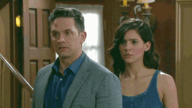 a man in a suit and a woman in a blue tank top stand next to each other