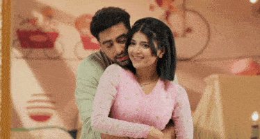 a man is hugging a woman in a pink sweater in a room .