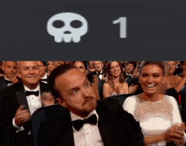 a man in a tuxedo is sitting in front of a crowd with a skull and the number 1