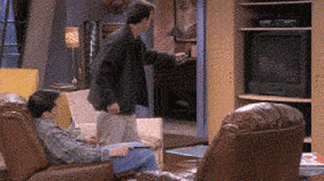 two men are sitting in chairs in a living room with a television in the background