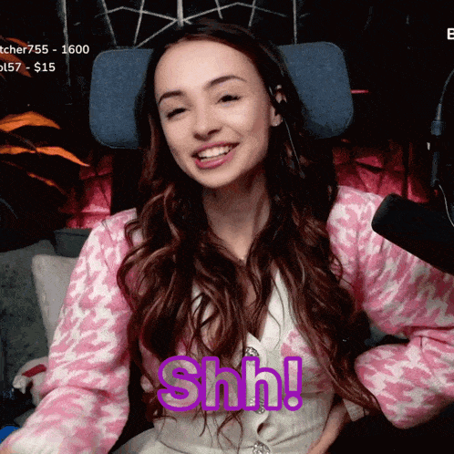 a woman in a pink and white sweater is smiling with the word shh behind her