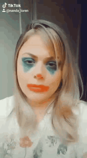 a woman with a clown makeup on her face has a tiktok account behind her