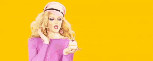 a woman blowing a pink donut while holding a small cupcake