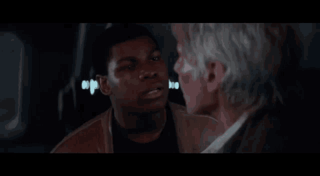 two men are standing next to each other in a dark room talking to each other .