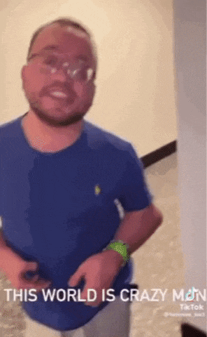 a man wearing glasses and a blue shirt is standing in a room with the words `` this world is crazy man '' .