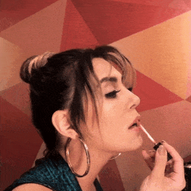 a woman with hoop earrings is applying lip gloss to her lips