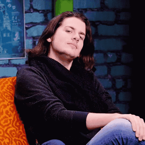 a young man with long hair is sitting on a couch