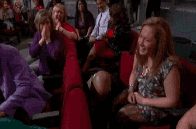 a group of people are sitting in red seats in a theater and applauding .