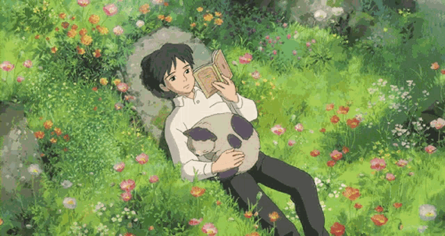 a man is laying in the grass reading a book while holding a cat