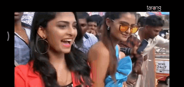 two women wearing sunglasses are standing in front of a crowd .