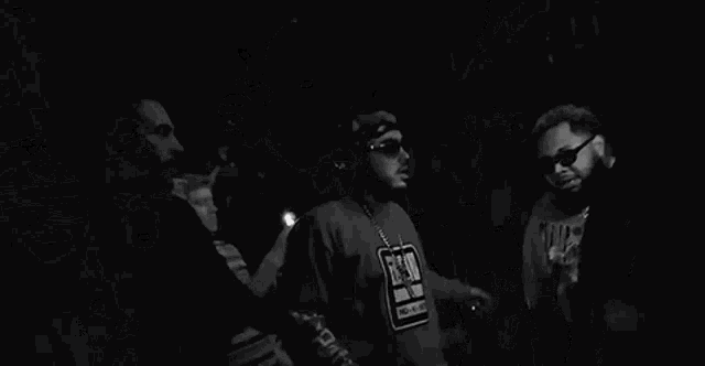 a group of men are standing in a dark room and one of them is wearing a shirt that says noble on the sleeve .