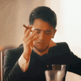 a man in a suit is smoking a cigar and drinking a glass of wine