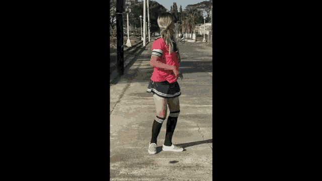 a woman wearing knee high socks and a pink shirt is standing on a sidewalk